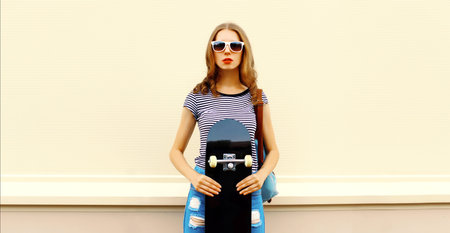Portrait of stylish young woman with skateboard in the city