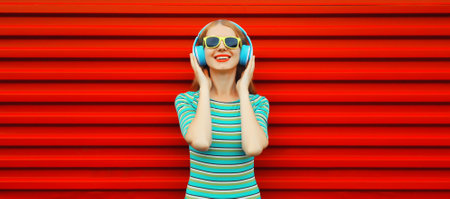 Portrait of happy smiling young woman in wireless headphones listening to music on red background