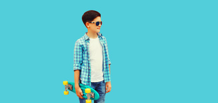 Portrait of teenager boy with skateboard looking away on blue background, blank copy space for advertising textの写真素材