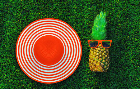 Summer vacation, fresh pineapple with sunglasses and round straw hat on the grass background, top viewの写真素材