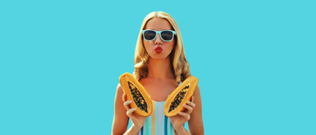 Summer sunny portrait of stylish young woman with fresh juicy papaya fruit blowing her lips sending...