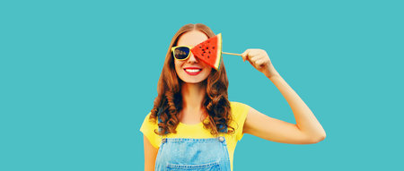 Summer portrait of happy cheerful young woman with fresh juicy fruits, lollipop or ice cream shaped slice of watermelon on blue backgroundの写真素材