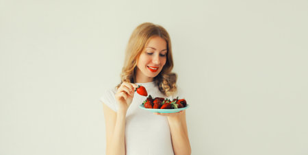 Portrait of happy smiling woman holding plate with fresh strawberries on white backgroundの写真素材