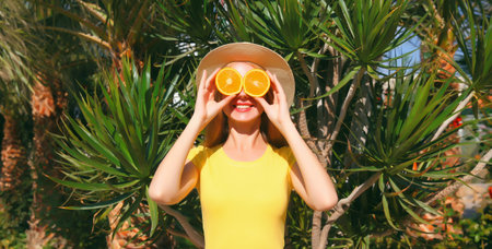 Summer, vacation, nutrition and vegetarian concept. Happy healthy cheerful young woman covering her eyes with slices of orange fruits and looking for something on beach with palm backgroundの写真素材