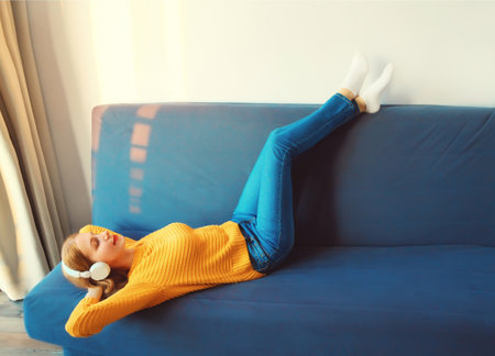 Happy relaxed young woman listening to music with wireless headphones with closed eyes lies on the...
