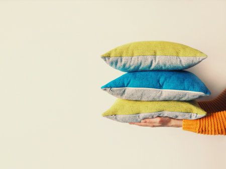 Healthy sleep, woman holding bunch of folded pillows on white wall at home