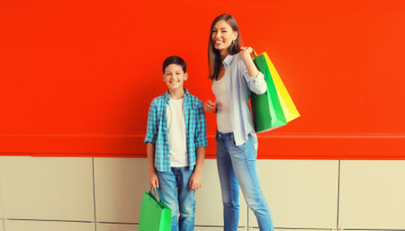 Happy smiling mother and son child together with shopping bags on red wall backgroundの写真素材