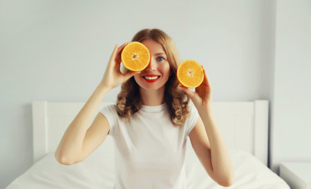 Summer, nutrition, diet and vegetarian concept. Happy healthy cheerful young woman with slices of orange fruits in white room at homeの写真素材