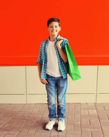 Happy smiling boy teenager with shopping bag in the city on red backgroundの写真素材
