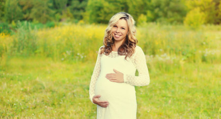 Portrait of happy young pregnant woman walking in summer parkの写真素材