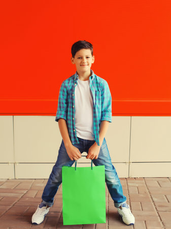 Happy smiling boy teenager with shopping bag in the city on red backgroundの写真素材