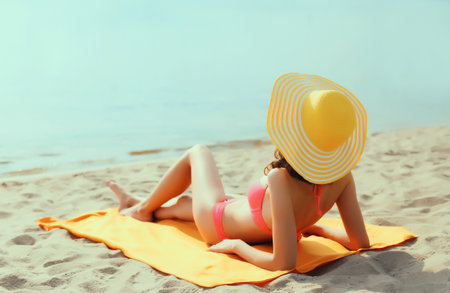 Summer vacation, happy relaxing young woman with straw hat lying on sand on the beach on sea...