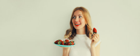 Portrait of happy smiling woman holding plate with fresh strawberries on white backgroundの写真素材