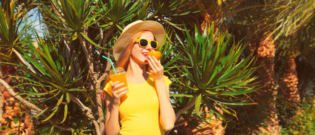 Summer portrait of happy young woman drinking fresh juice wearing straw hat on the beach with palm tree backgroundの写真素材