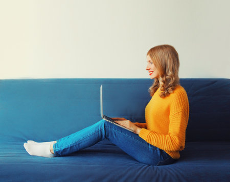 Modern young woman working with laptop sitting on the couch in the room at homeの写真素材