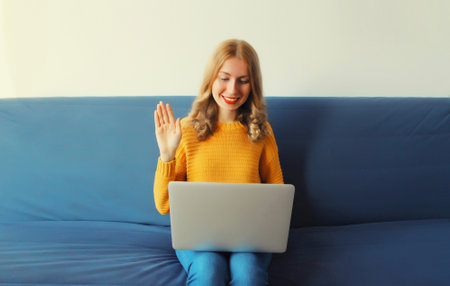 Happy smiling young woman working with laptop welcomes communicates via video call sitting on the...