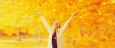 Happy laughing woman having fun with flying yellow leaves in autumn parkの写真素材