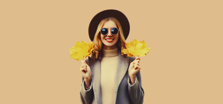 Autumn color style outfit, portrait of beautiful smiling young woman with yellow maple leaves...