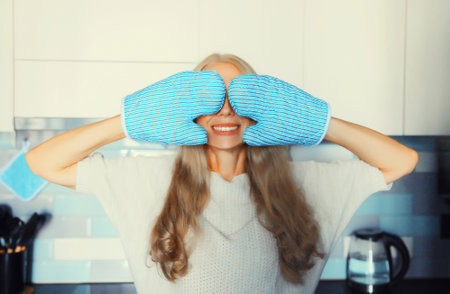 Surprised excited cheerful middle-aged woman housewife with oven gloves potholders having fun doing housework in the kitchen at homeの写真素材