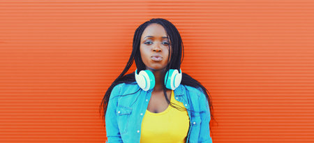 Portrait of young african woman listening to music in headphones on orange backgroundの写真素材