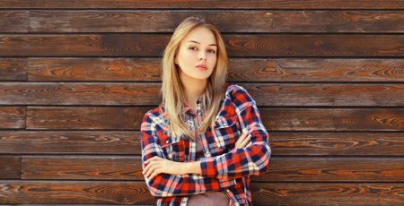 Portrait of beautiful confident caucasian blonde young woman with crossed arms in casual checkered shirt in the cityの写真素材