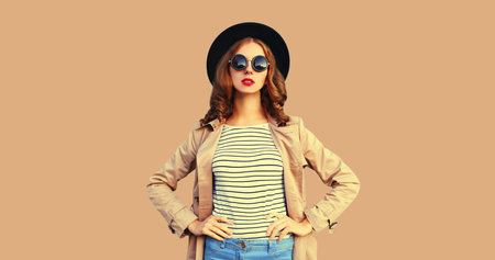 Portrait of beautiful woman posing wearing black round hat, coat jacket isolated on brown studio...
