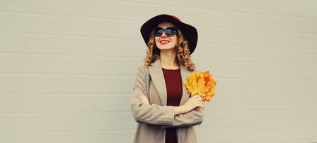 Autumn color style outfit, beautiful elegant smiling woman with yellow maple leaves wearing hat and...