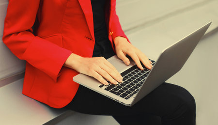 Businesswoman working with laptop in the city wearing red blazer jacket, close up woman's hands typing text on the keyboard pc computerの写真素材