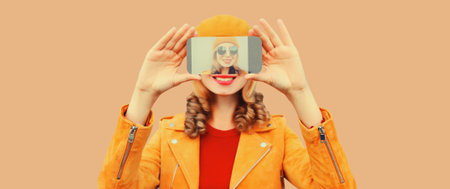 Close up of stylish young woman stretching her hands taking selfie on smartphone wearing orange...