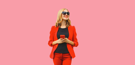Beautiful elegant lady business woman with mobile phone wearing red blazer on pink studio backgroundの写真素材