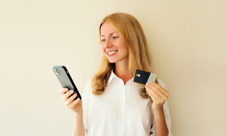 Happy caucasian young woman shopping online or ordering something looking at smartphone holding...