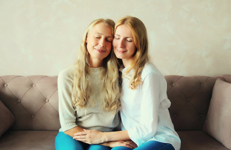 Portrait of happy smiling caucasian middle aged mother hugging her adult daughter together sitting...