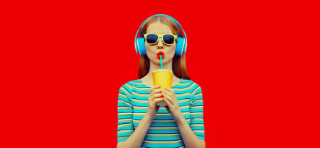 Fashion portrait of stylish young woman listening to music with headphones drinking fresh juice...