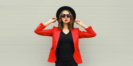 Stylish elegant woman posing in business suit, red blazer jacket and black round hatの写真素材