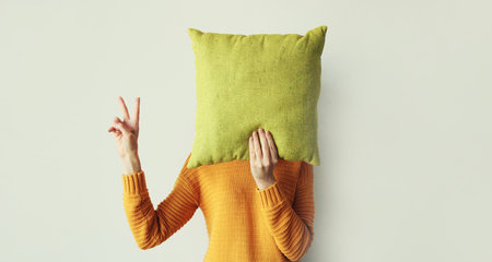 Healthy sleep, woman covering her head with colorful soft pillow holding in hands at home in morningの写真素材