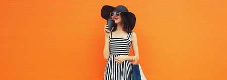 Stylish beautiful happy young woman model with shopping bags in summer black straw hat, striped...