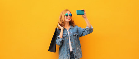 Portrait of beautiful happy smiling young woman taking selfie with phone holding black shopping bags...