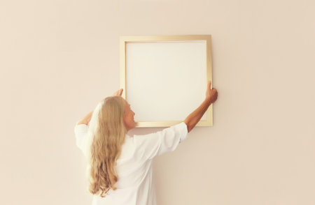 Woman decorating interior, hanging white blank photo frame, wooden picture, artwork mockup on wall in new houseの写真素材