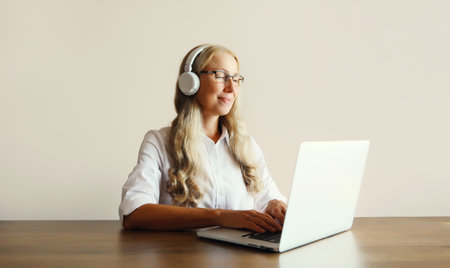 Happy relaxing middle aged woman listening to music in headphones working with laptop computer...