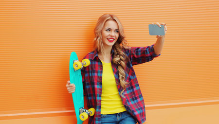 Summer portrait of happy smiling blonde young woman taking selfie with smartphone and skateboard on...