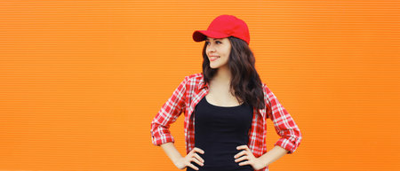 Summer portrait of happy smiling young woman posing in red baseball cap, casual clothes on city...