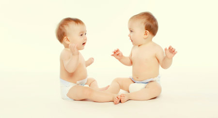 Cute two twin babies in diapers sitting on the floor on white studio backgroundの写真素材