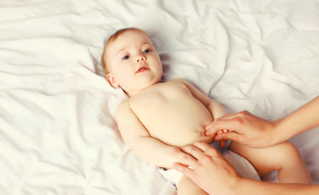 mother gives massage to baby lying on the bed at home, child and health conceptの写真素材