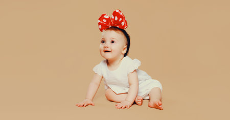 happy cute baby with bow on the head crawling on the floor on brown studio backgroundの写真素材