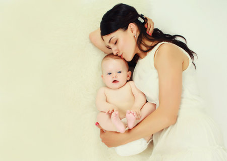 happy young mother lying with baby together on the floor at homeの写真素材