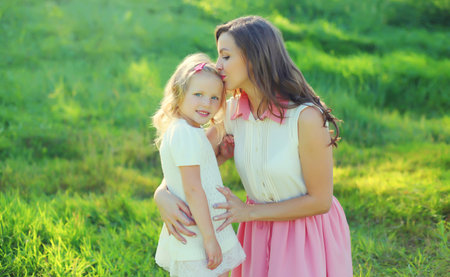 Portrait of happy cheerful smiling mother with little girl child daughter on the grass in sunny summer parkの写真素材