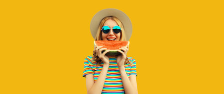 Summer portrait of happy young woman eating fresh slice of watermelon in straw tourist hat, sunglasses on colorful yellow studio backgroundの写真素材