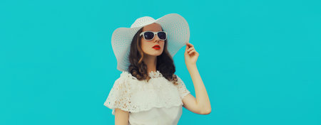 Portrait of beautiful caucasian young woman model posing wearing white summer straw hat on blue...