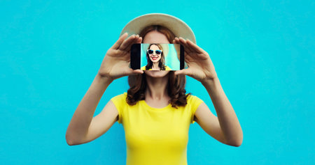 Close up portrait of woman taking selfie with mobile phone stretching her hands on colorful blue backgroundの写真素材