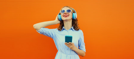 Portrait of happy smiling young woman listening to music in headphones with smartphone on bright...